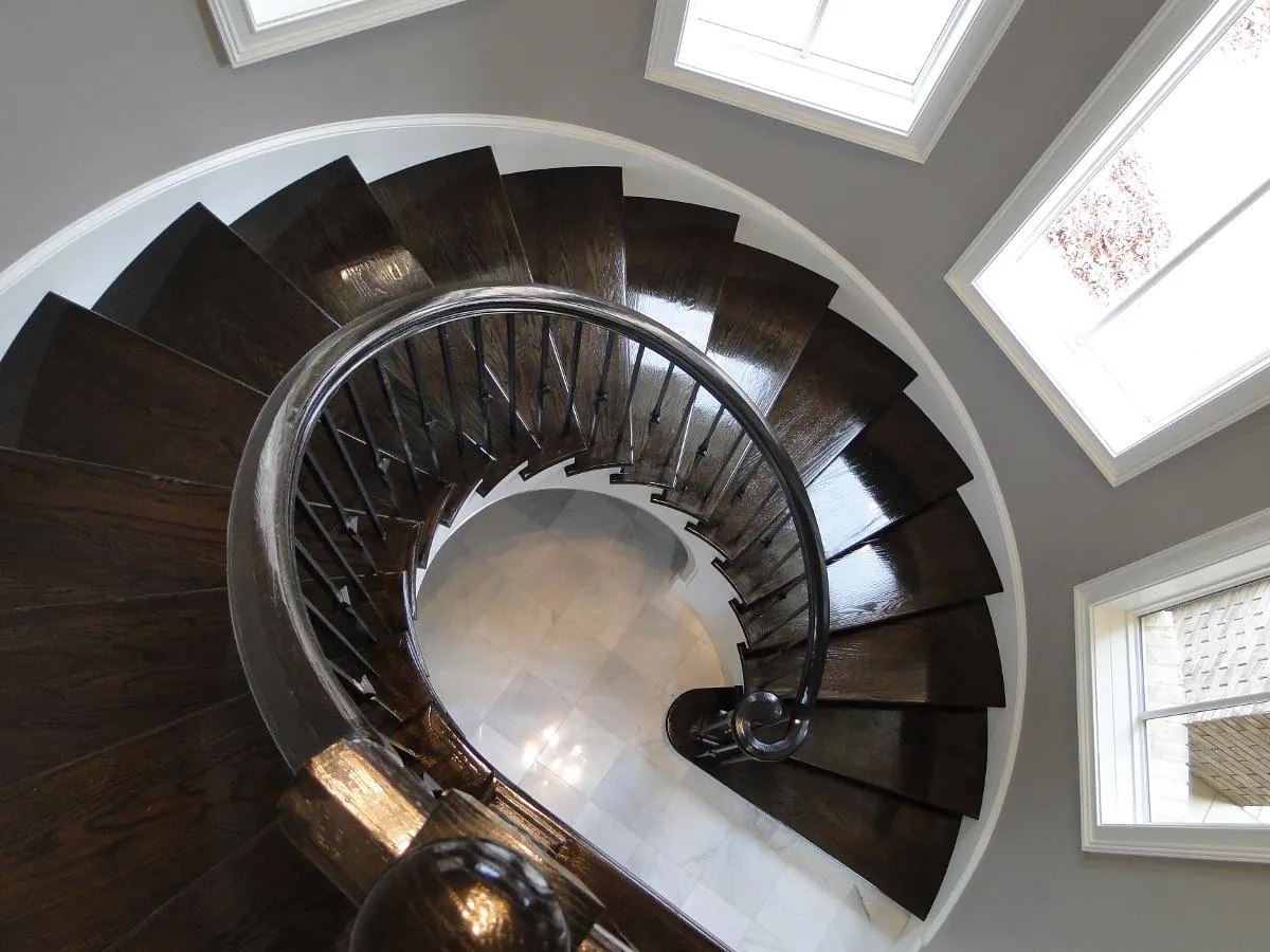 Dark-stained circular staircase photographed from above, descending in a tight spiral.